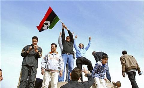 Người dân đứng trên 1 chiếc xe tăng giương cao 1 lá cờ thời  kỳ tiền Gadhafi tại Benghazi, Libya, 21/2/2011