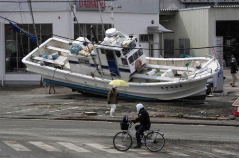 Một người đạp xe đi qua một con thuyền đánh cá bị kéo giạt lên bờ ở Sendai. Ảnh: AP.