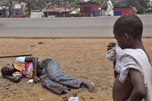 Một đứa trẻ đang bịt mũi đứng nhìn người đàn ông nghi nhiễm virus Ebola đang nằm vạ vật tại một phố chính của khu đông dân cư ở Monrovia, Liberia vào thứ 6 ngày 12 tháng 9 năm 2014. (Ảnh Abbas Dulled)